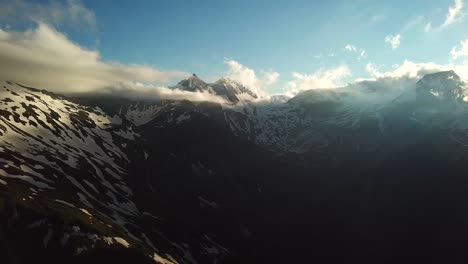 Aerial-landscape-view-of-sun-rays-through-a-cloudscape-over-austrian-mountains-snowy-peaks