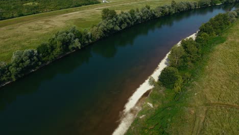 sunlit riverbank with sand and grass beside calm water in summer