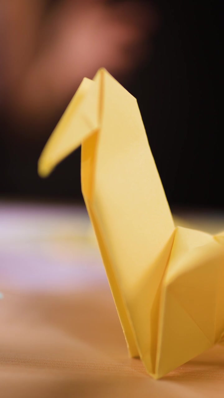 Close-up shot of a completed yellow paper crane standing on a wooden table indoors