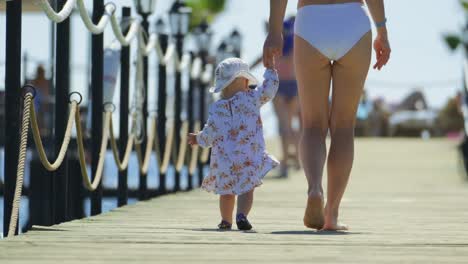 rear view of a mother with her little daughter are walking on a wooden pier by the sea