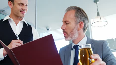 Man-tasting-the-wine-and-waiter-suggesting-the-menu-to-him-