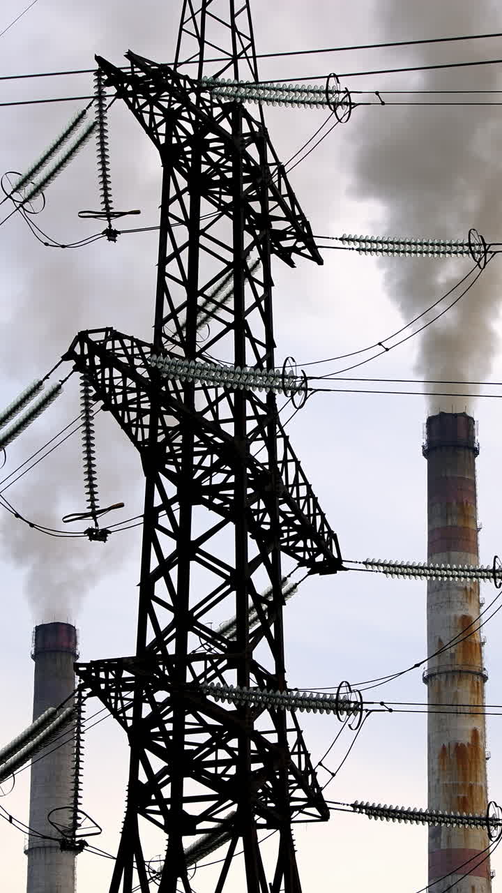 Problem of environmental pollution and air. High voltage towers and massive smoke from industrial pipes on the sky background. Vertical video