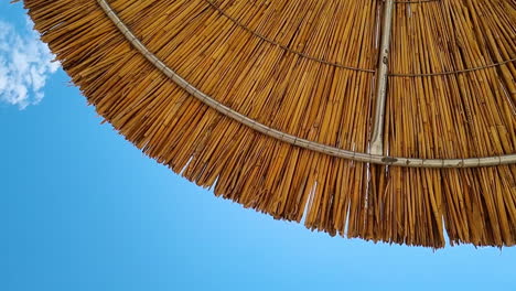 Vista-Giratoria-De-Abajo-Hacia-Arriba-Bajo-La-Sombrilla-De-Playa-De-Paja-De-Caña-Y-Cielo-Azul-Claro-En-Un-Día-Soleado