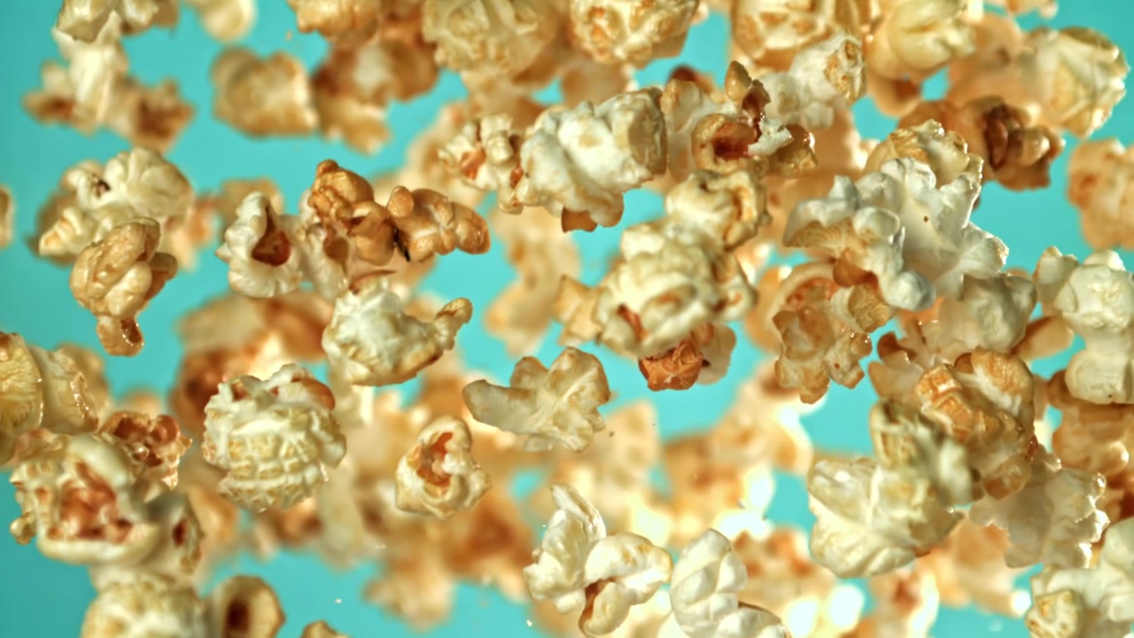 Caramel Popcorn Flying and Falling in Slow Motion on a Teal Background