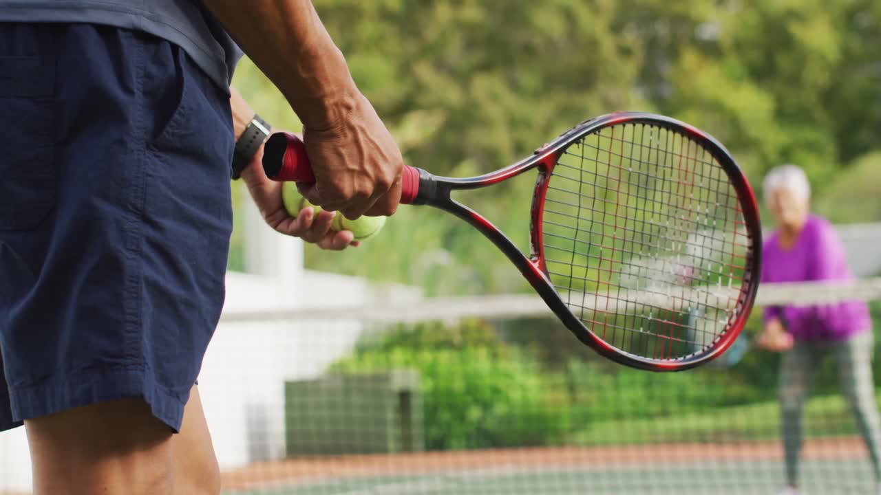 Video of hands of biracial senior man holding racket and starting match on tennis court