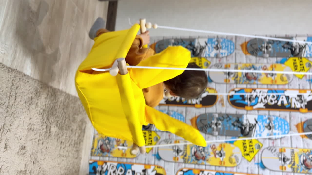 Happy smiling baby boy sitting in a yellow swing. Mom's hands pushing a swing. Fun at home. Vertical screen.