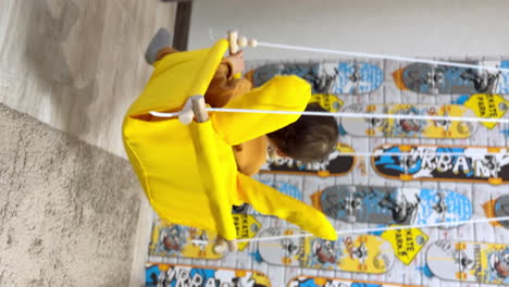 happy smiling baby boy sitting in a yellow swing. mom's hands pushing a swing. fun at home. vertical screen.