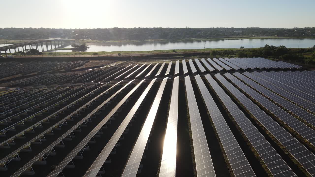 воздушный вид, летящий по рядам фотоэлектрических солнечных панелей вдоль деревенской реки на закате