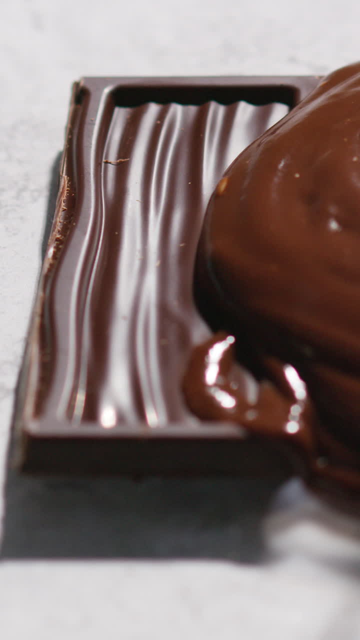 video vertical de chocolate derretido siendo vertido sobre una pieza de barra de chocolate contra un fondo blanco