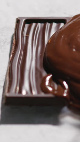 vertical video of melting chocolate being poured onto piece of chocolate bar against white background