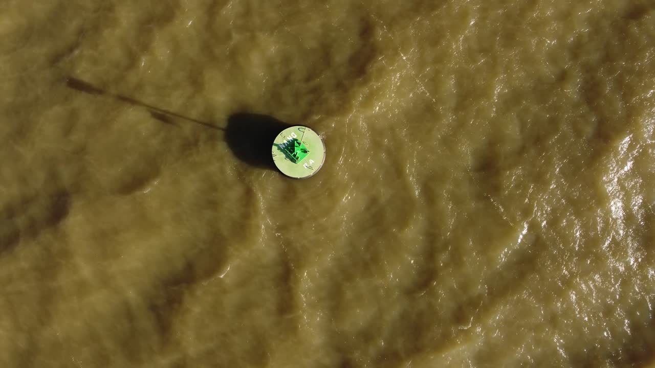 Aerial top view showing Green buoy floating on brown water of Parana River at sunset