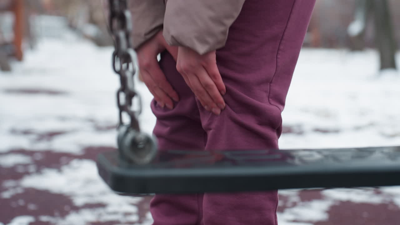 겨울 옷을 입은 사람이 왼쪽 무을 고, 아마도 통증이 있고, 근처에 스이 있고, 손이 갈색 바지를 누르고, 불편함을 암시하고, 흐릿한 배경은 멀리서 스하는 사람을 보여줍니다.