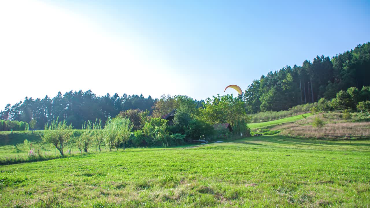 Paraglider pilot flying over green grass, approaches as birds fly away