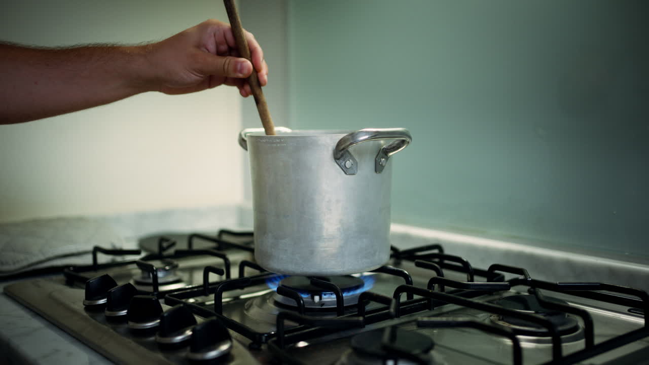 Person adjusting stove with pot for cooking, indoor kitchen setting