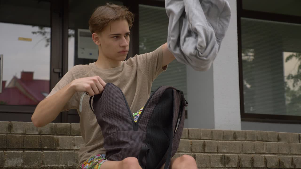 подросток достает из рюкзака джемпер и пытается его надеть
