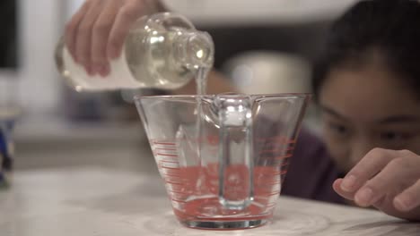 a young korean girl pours syrup into a measuring cup while baking cookies