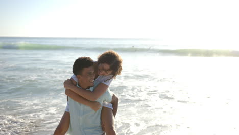 Biracial-couple-enjoys-a-piggyback-ride-on-a-sunny-beach-with-copy-space