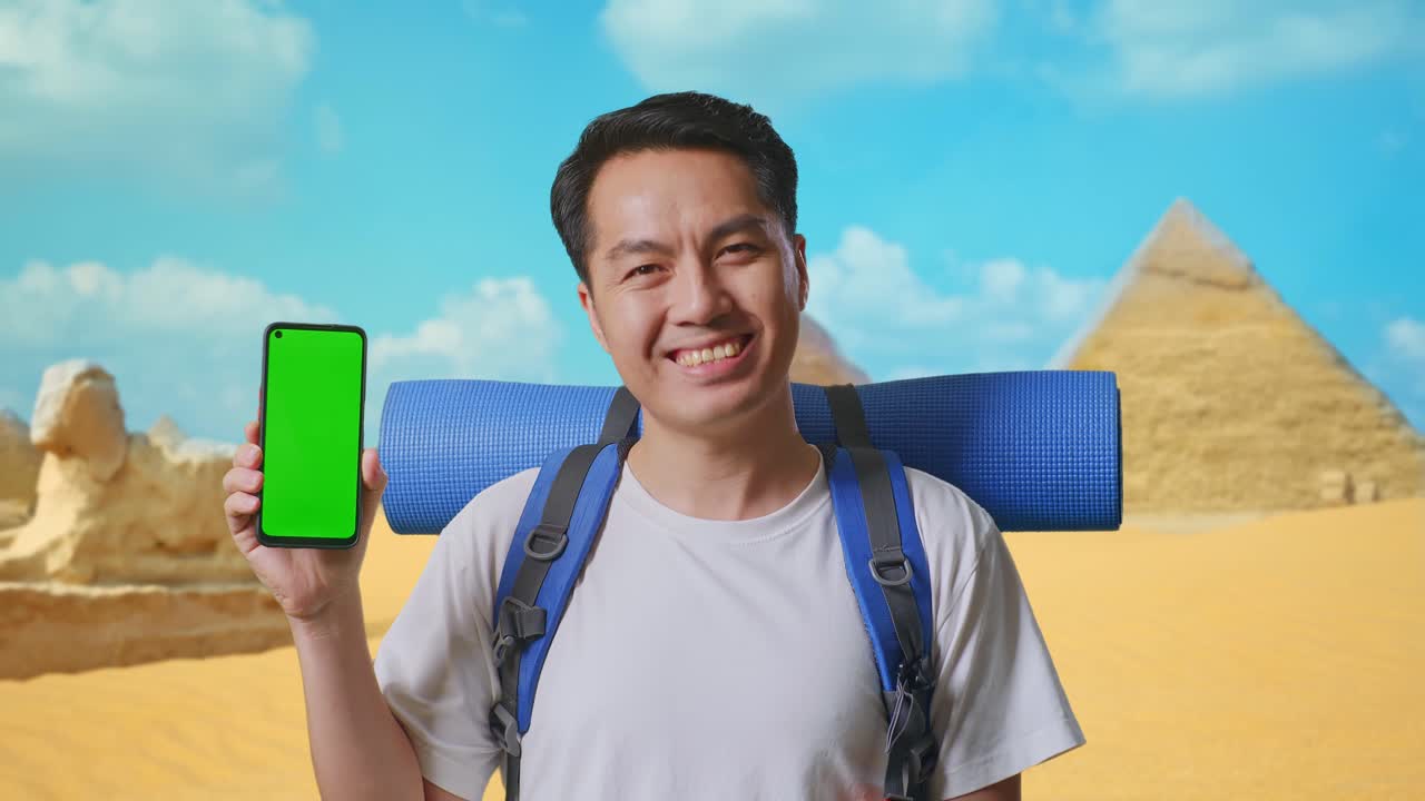 Close Up Of Asian Male Hiker With Mountaineering Backpack Smiling And Showing Mock Up Green Screen Smartphone While Traveling In Pyramid Of Giza
