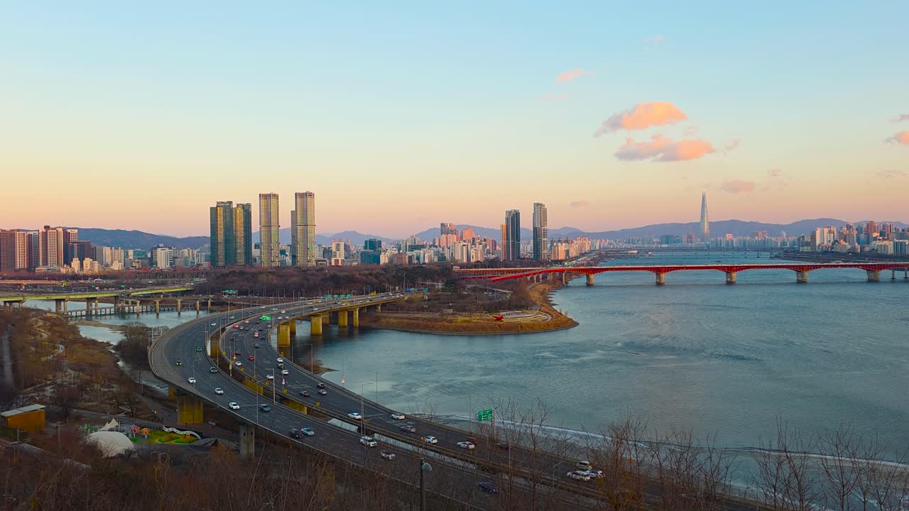 Ripresa aerea in tempo reale del traffico della superstrada curva Gangbyeonbuk-ro al tramonto dorato, con il ponte Seongsu rosso, la Lotte Tower e lo skyline di Seoul sul fiume Han