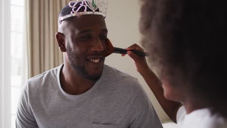 african american father wearing tiara having makeup put on by his daughter