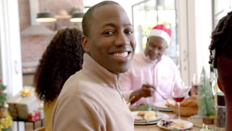 happy african american father smiling at multi generation family christmas dinner table