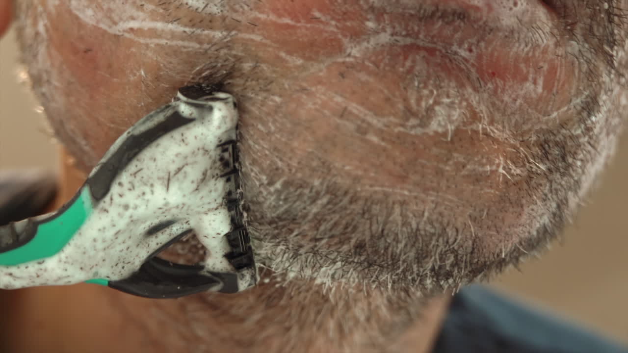 Close-up van een man die zijn baard scheert met een groen en zwart scheermes