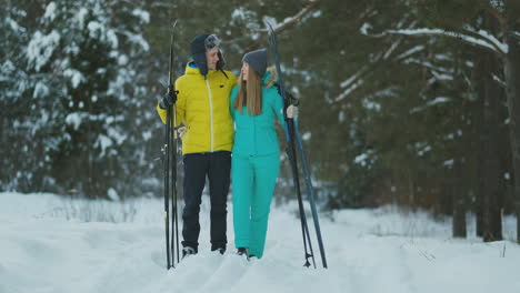 full length portrait of caring young man helping injured girlfriend during ski walk in winter forest