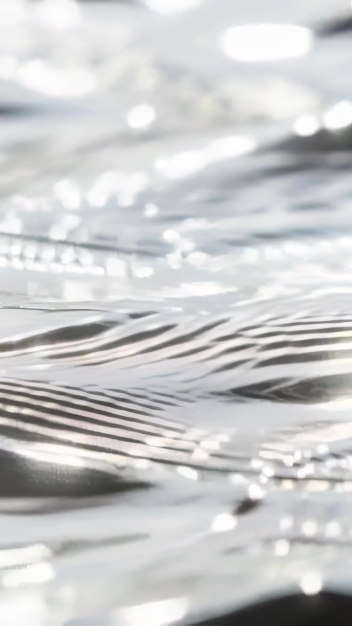 Video verticale: Luce solare splendente sull'acqua increspata di uno stagno che crea increspature, mostrando riflessi bokeh.