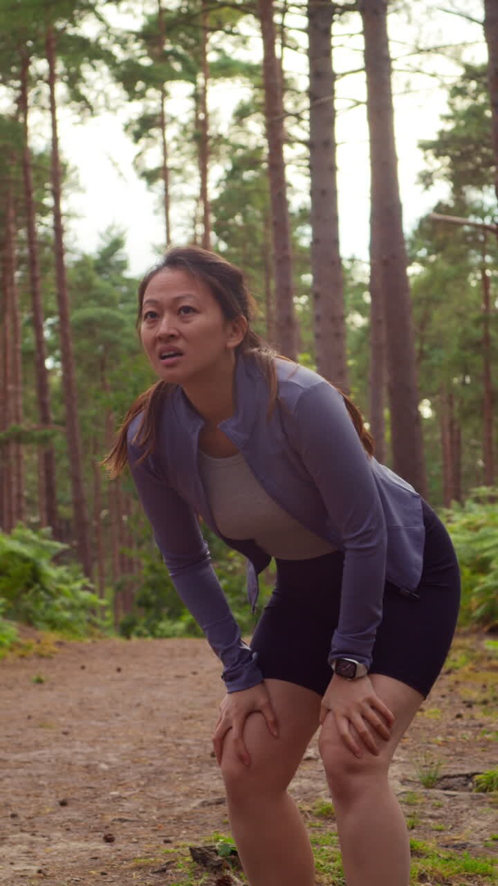 Video verticale di una donna che si allena all'aperto, correndo lungo un sentiero nel bosco e fermandosi per riprendere fiato, ripreso in tempo reale 1
