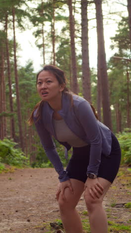 Video-Vertical-De-Una-Mujer-Haciendo-Ejercicio-Al-Aire-Libre-Corriendo-Por-Una-Pista-En-El-Bosque,-Deteniéndose-Para-Tomar-Aire,-Filmado-En-Tiempo-Real-1