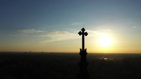 an aerial shot of a cathedral's steeple with a cross on it, during sunrise