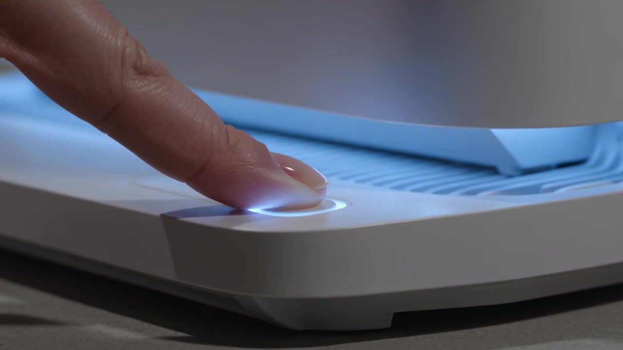 Pressing adult fingertip contacting round button on desk, activating device LED ring and blue glow