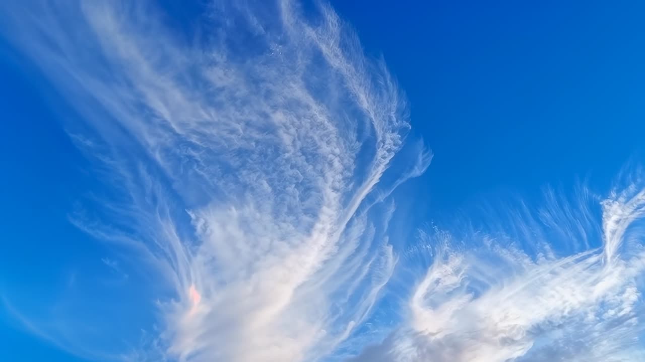 Driftende Federwolke, die sich am spätnachmittäglichen blauen Himmel ausdehnt und dünner wird, angetrieben von Höhenwinden.