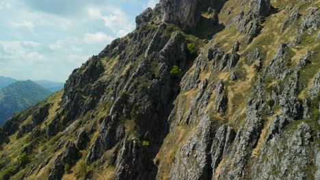 Aerial-scenic-view-of-a-rocky-mountain-peak-with-lush-greenery-under-a-clear-blue-sky,-perfect-for-outdoor-enthusiasts