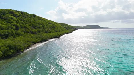 Light-glistens-on-turquoise-water-as-dry-Caribbean-island-vegetation-rolls-to-the-beach-shoreline