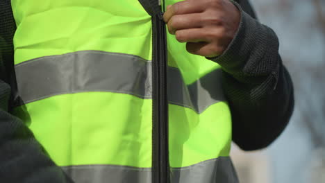 close-up view of unzipped high visibility safety vest in fluorescent yellow with silver reflective stripes, showing detailed black zipper and textured dark inner clothing, designed for protective outdoor