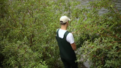 toma en cámara lenta de un pescador que usa vadeadores caminando por los arbustos hasta el río para pescar con mosca