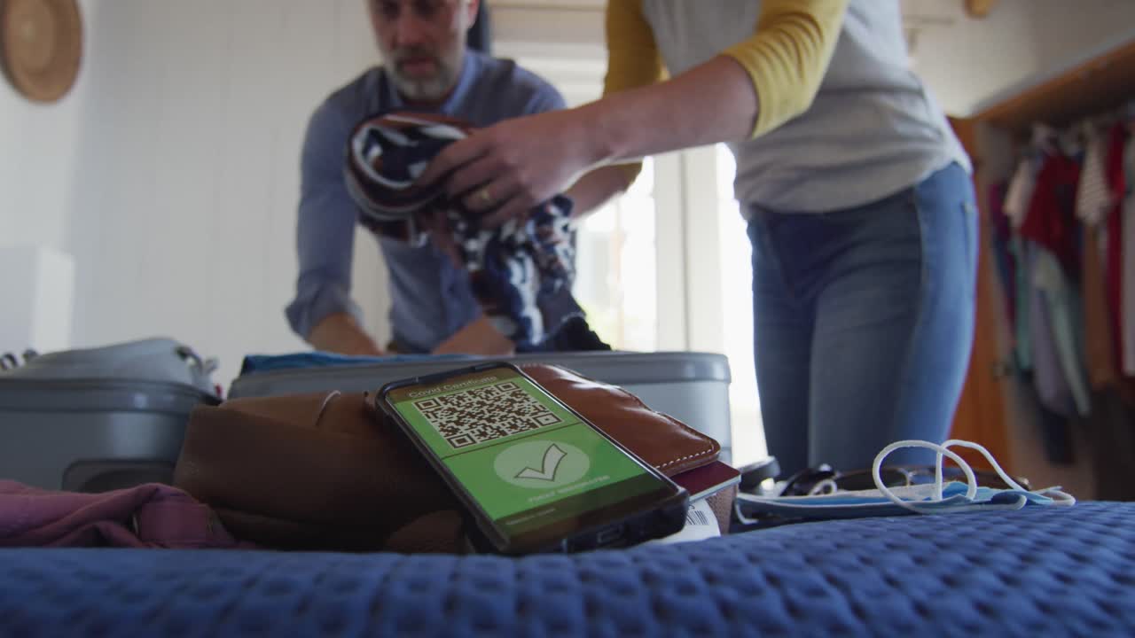 feliz pareja caucásica madura empacando máscaras faciales y teléfono inteligente con pasaporte de vacuna contra el covid-19