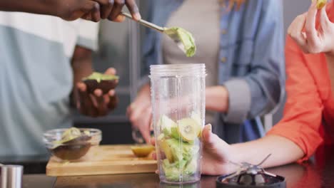 midsection of group of diverse friends preparing healthy drink in kitchen together