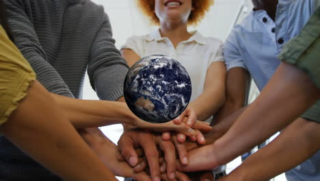 animation of rotating globe over excited multiracial coworkers stacking hands at office