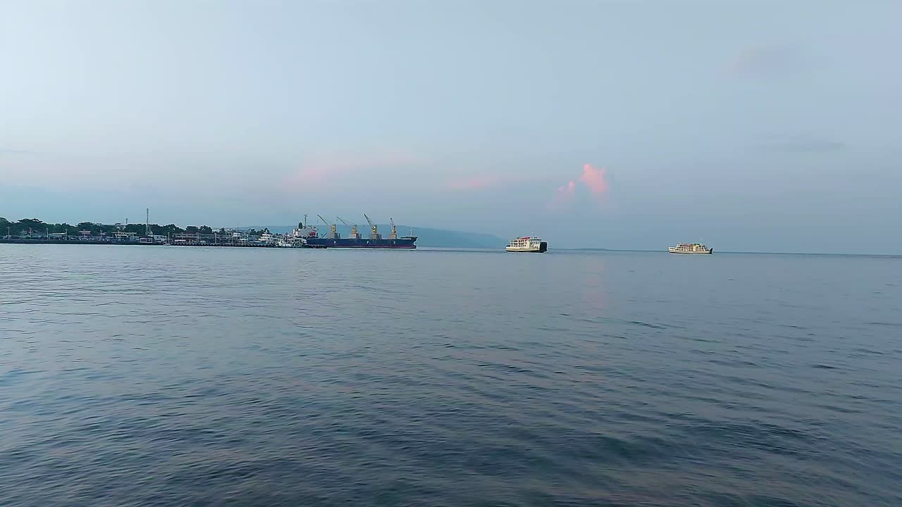 Vast view of the open sea with the harbor and moored boat in the horizon