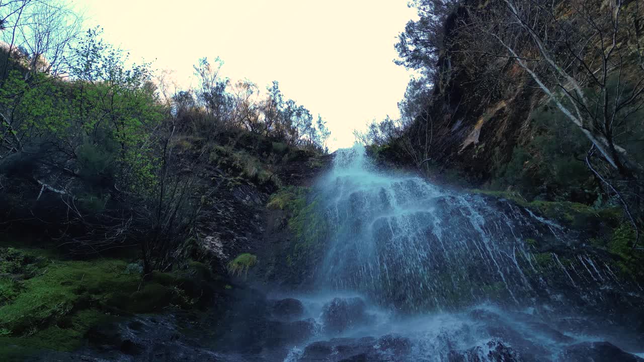Fervenza da Pedreira In Lugo, Spain - Cascading Waterfall Surrounded By Rugged Cliffs And Dense Trees. drone pullback, low angle shot