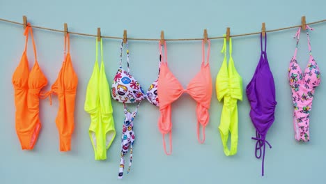 a vibrant display of colorful swimwear hanging on a clothesline, showcasing a summer collection of brightly colored bikinis and one-piece swimsuits