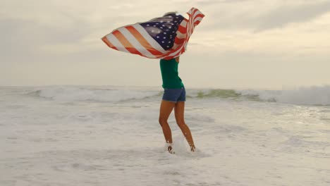 front view of african american woman with waving american flag dancing on the beach 4k