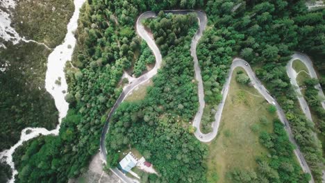 Bird's-eye-drone-shot-with-a-sideways-movement-of-a-winding-road-inside-a-forest-and-cars-passing-by