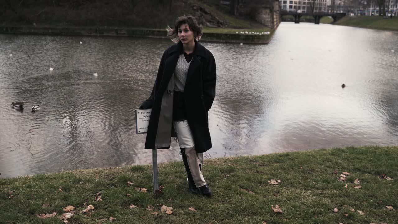 молодая женщина в черном пальто стоит в парке у моря осенью во второй половине дня