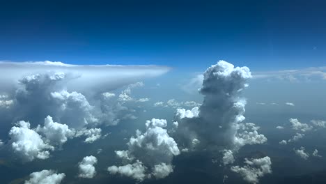 an immersive pilot’s view taken from a jet cockpit while flying above storm clouds under an intense blue sky, with an anvil shape cumulonimbus on the left.