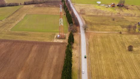 Aerial-view-looking-down-over-single-green-tractor-travelling-rural-agricultural-Latvian-countryside-road-between-farmland