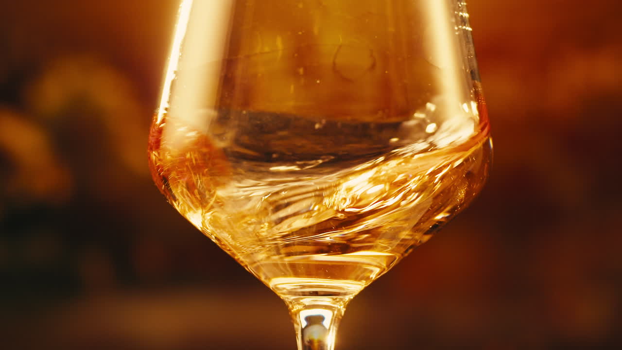 Orange or white wine bottle and glass against a sunset in a peaceful vineyard, pouring of ecological natural wine.