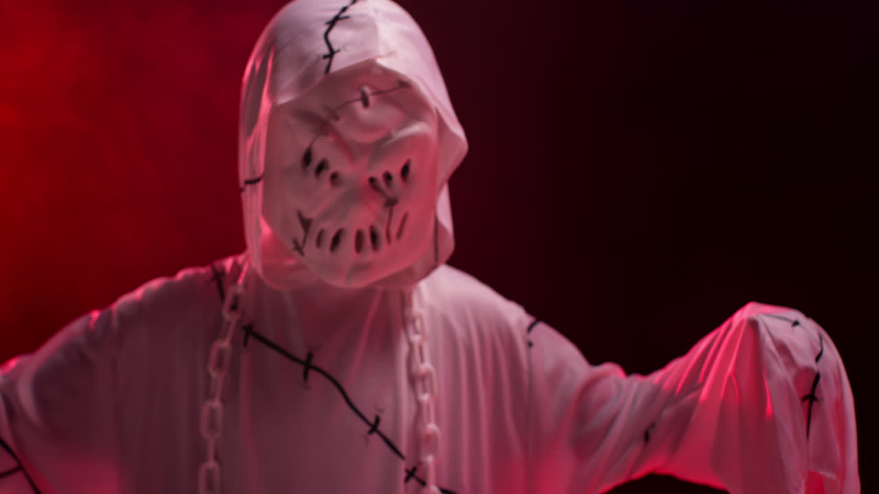 Child Dressed Up In Ghost Zombie Monster Costume Trick Or Treating At Halloween Scaring People Against Red Smoke Background